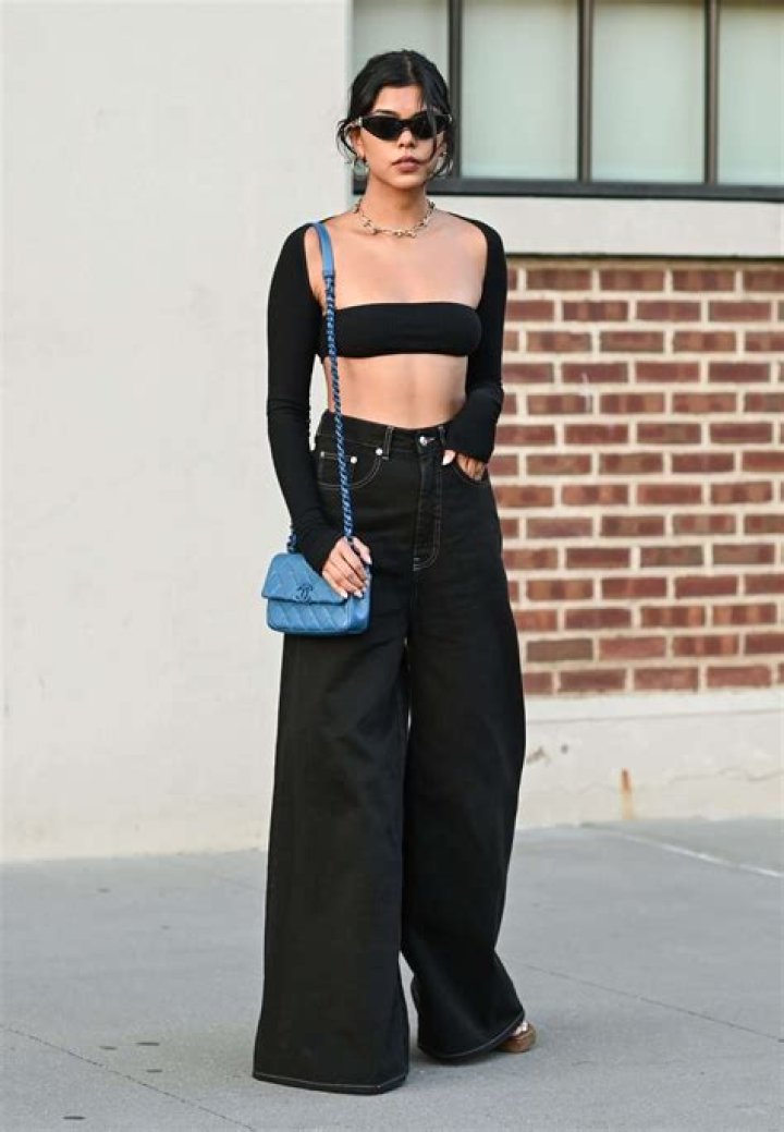 A woman wearing black, baggy wide-leg cotton ankle length overalls with a white long-sleeve shirt underneath